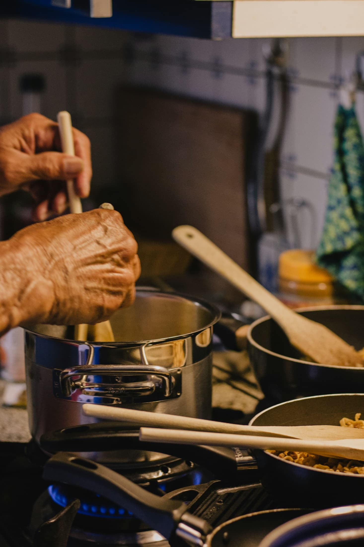 A pair of weathered hands stirring a pot on the stove in warm kitchen light